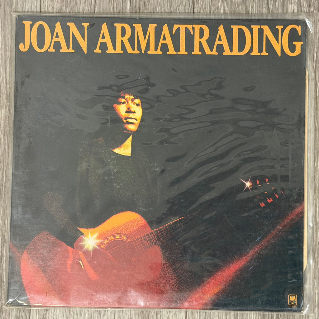 Vinyl record cover with a person holding a guitar and the text 'Joan Armatrading' on a reflective surface.