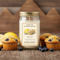 Jar of lemon and blueberry muffin-scented candle with muffins and lemons on a wooden surface